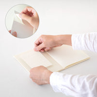 Person applying a sheet of paper to a notebook on a white surface.